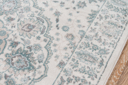 Cream rug with blue-green ornamental medallion pattern and bordered edge on wood floor.