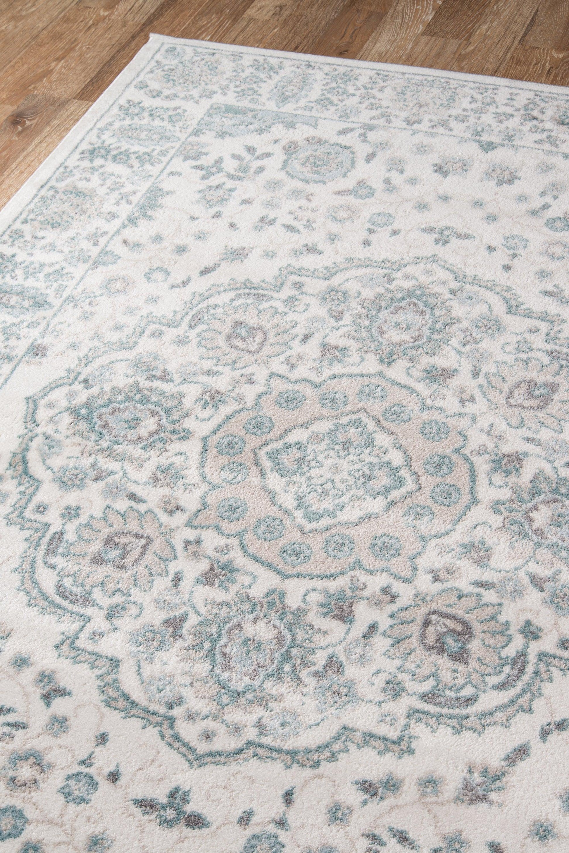 Ivory rug with teal floral and medallion pattern on a wooden floor.
