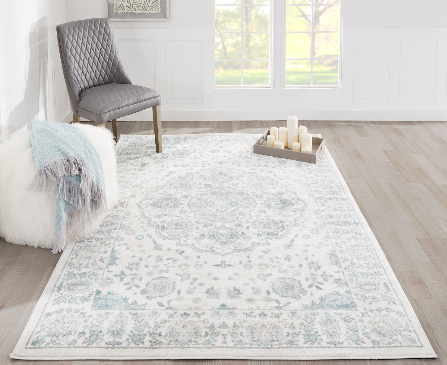 Ivory-blue Persian rug with a gray-blue border in a bright living room, paired with a quilted gray chair and fluffy throw.