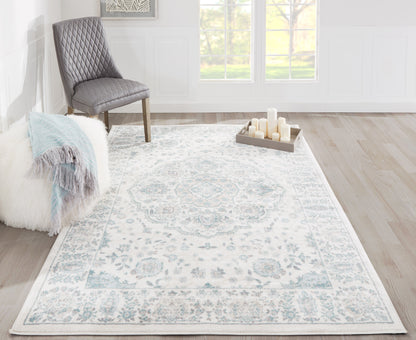 Ivory-blue Persian rug with a gray-blue border in a bright living room, paired with a quilted gray chair and fluffy throw.