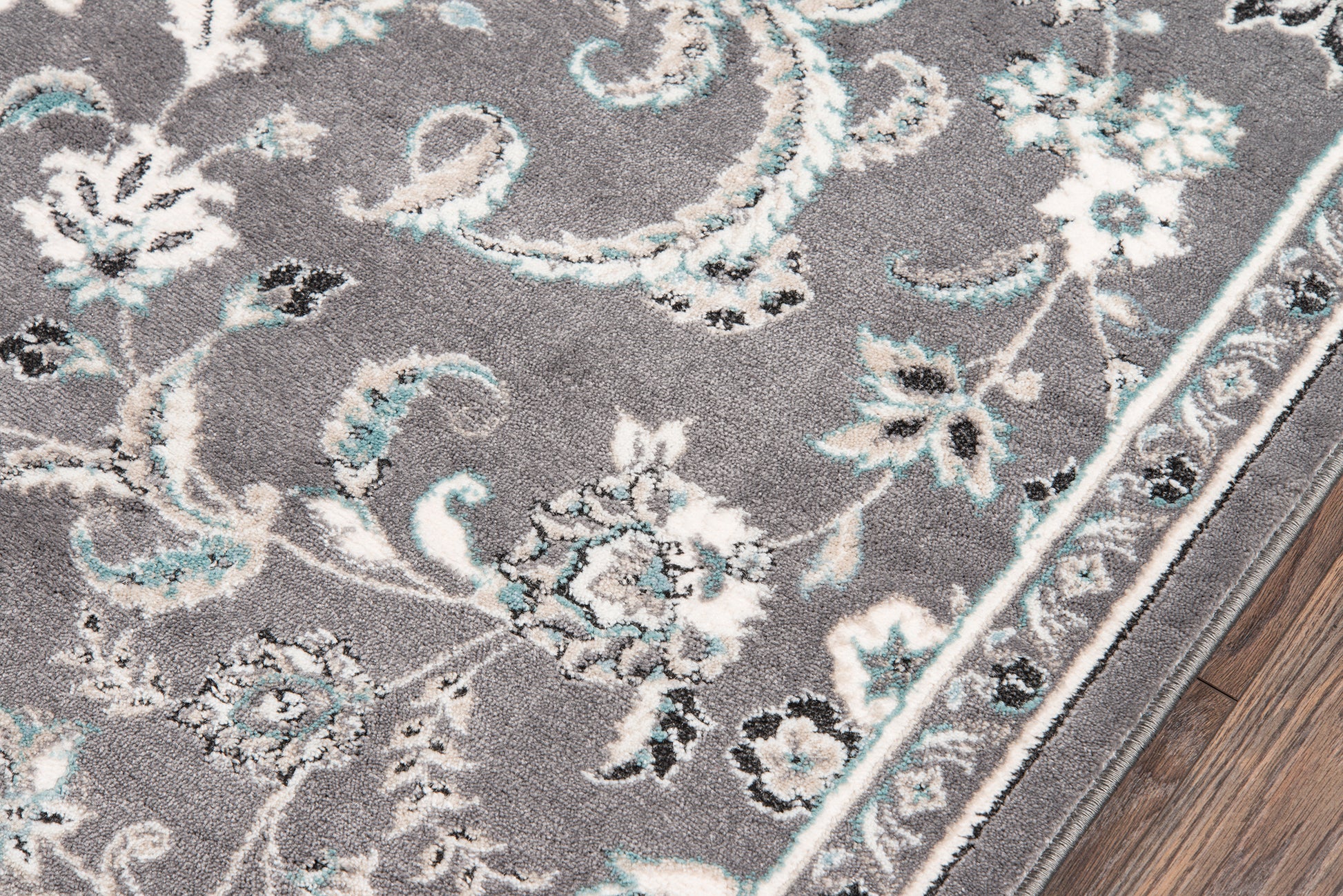 Rectangular gray ornate floral area rug with white and turquoise accents and a decorative border on a wood floor, size 9' x 13'.