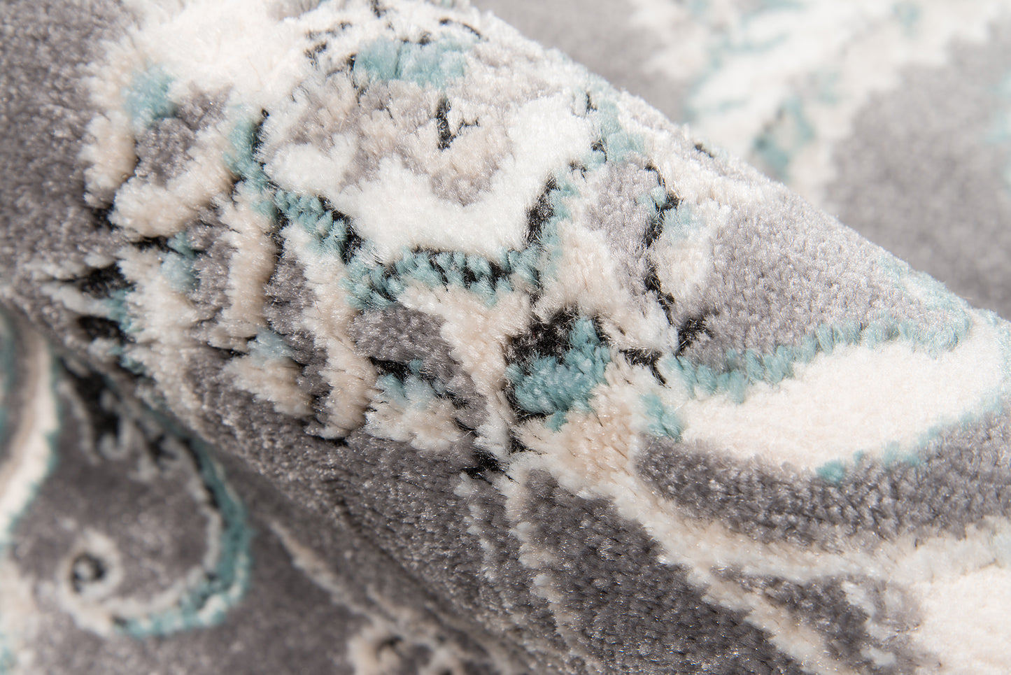 Close-up of a grey plush rug with cream and mint pattern, textured pile and ornate geometric motif.