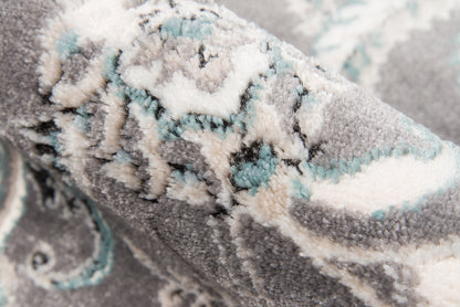 Close-up of a grey plush rug with cream and mint pattern, textured pile and ornate geometric motif.