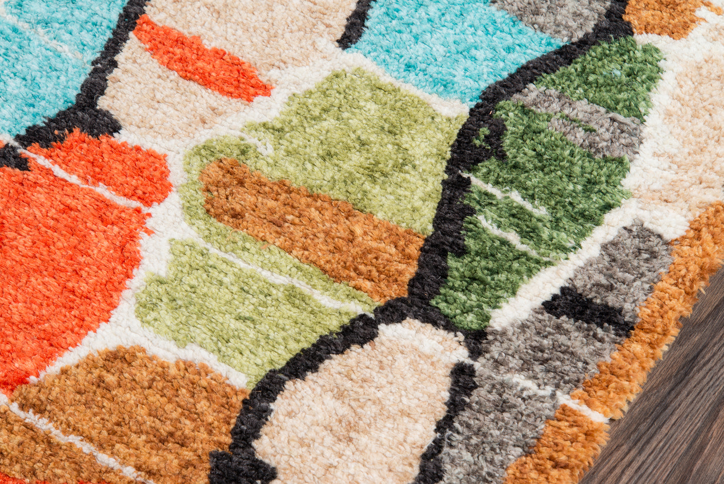Colorful tufted area rug with abstract geometric blocks in turquoise, orange, lime green, beige and black outlines on wood floor.
