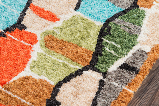 Colorful tufted area rug with abstract geometric blocks in turquoise, orange, lime green, beige and black outlines on wood floor.