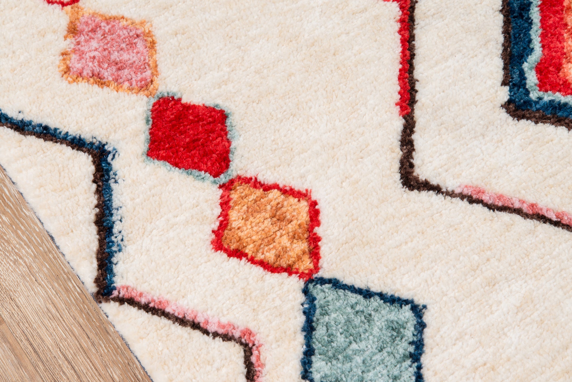 Cream shag rug with geometric squares in red, orange, teal and blue on light wood floor.