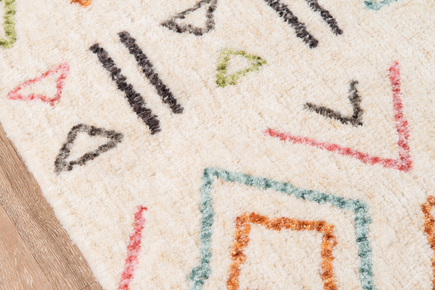 Cream plush rug with colorful geometric shapes, teal border and orange frame, red lines and black accents on wood floor