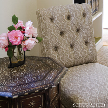 Beige damask tufted chair with button detailing beside a dark octagonal wood side table with a mosaic top & pink flowers