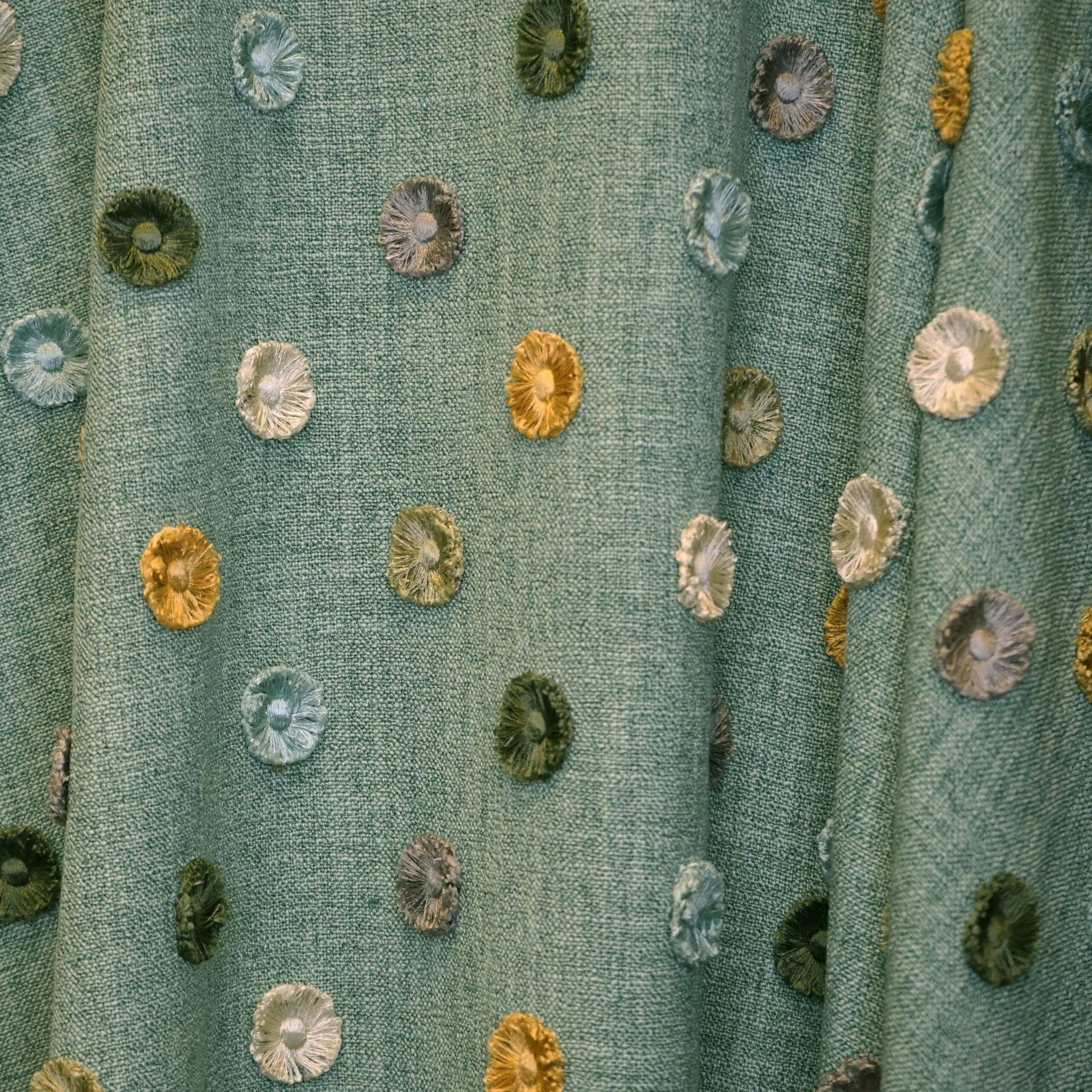 Teal woven fabric with scattered multicolor circular button-like embroidery patches in blues, greens, yellows.