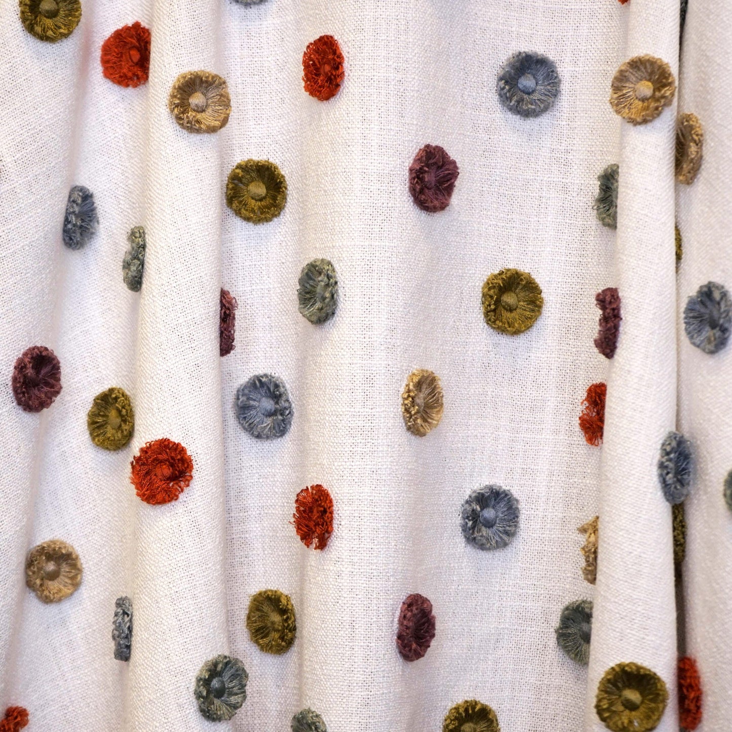 Cream fabric swatch with multicolor dot pattern in red, mustard, gray, blue and green.