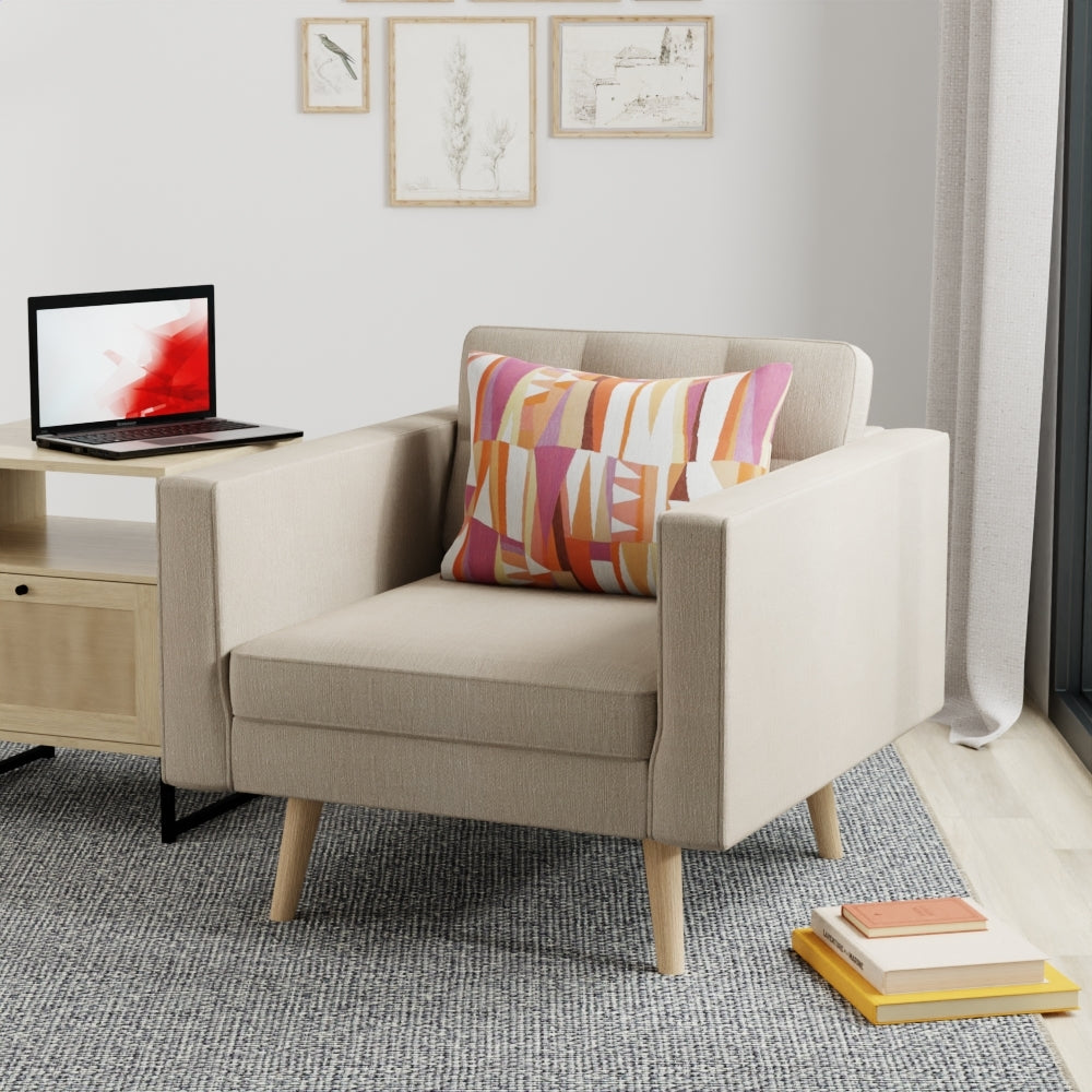 Beige fabric mid-century armchair with wooden legs and a colorful geometric pillow in a modern living room.