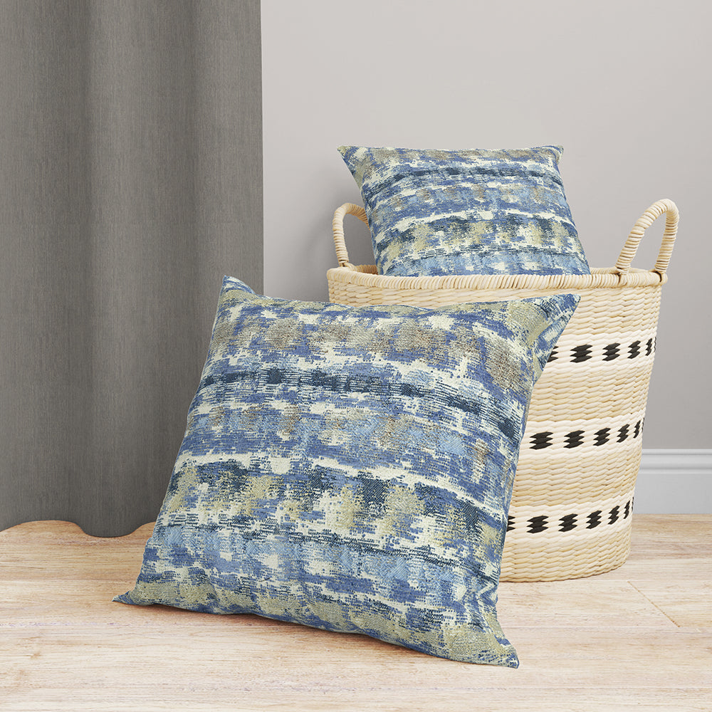 Two blue-gray denim transitional fabric pieces; one on the floor, the other in a woven striped straw basket, coastal rustic decor.
