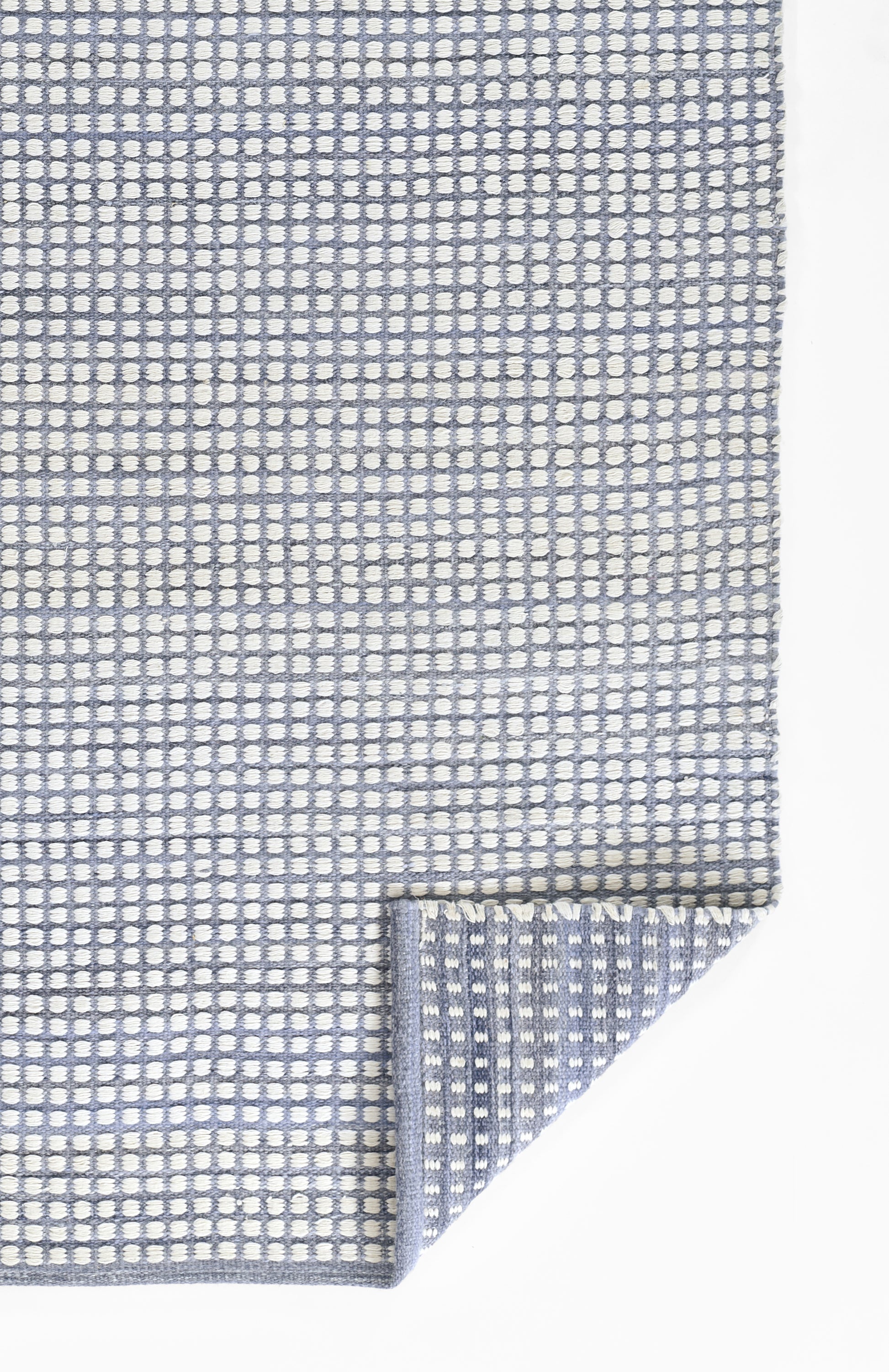 Blue and white woven rug with a small dotted grid pattern, rectangular with a folded corner.