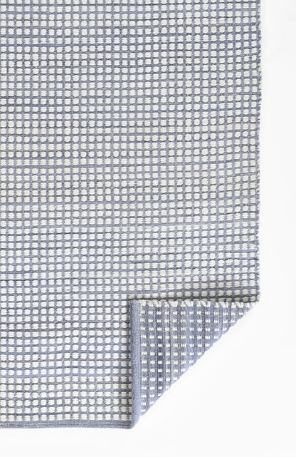 Blue and white woven rug with a small dotted grid pattern, rectangular with a folded corner.