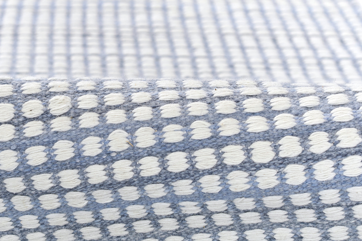 Blue woven rug with white tufted dots in a grid pattern; soft textured home decor.