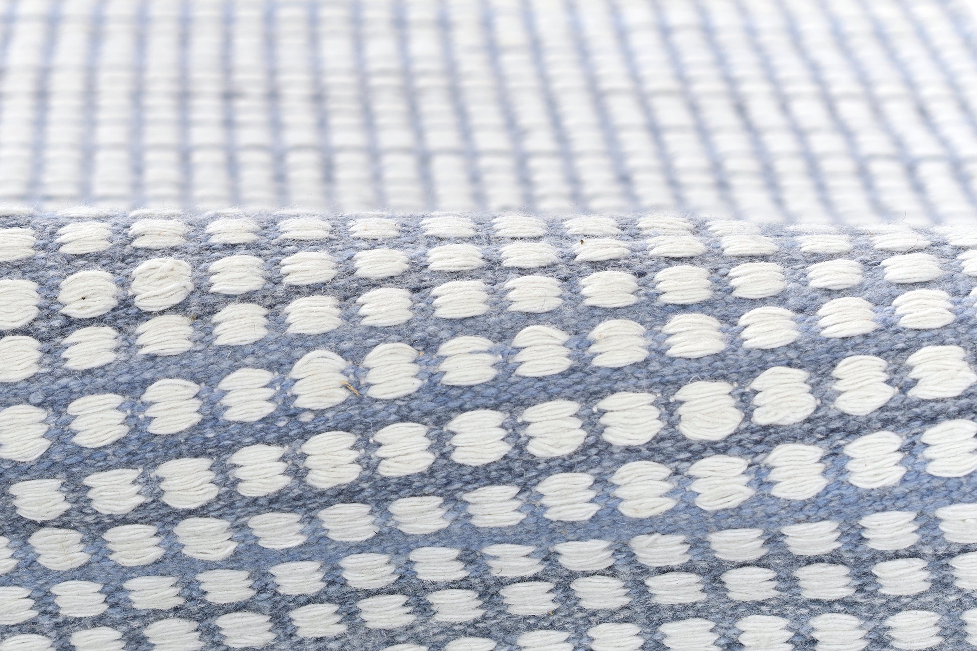 Blue woven rug with white tufted dots in a grid pattern; soft textured home decor.