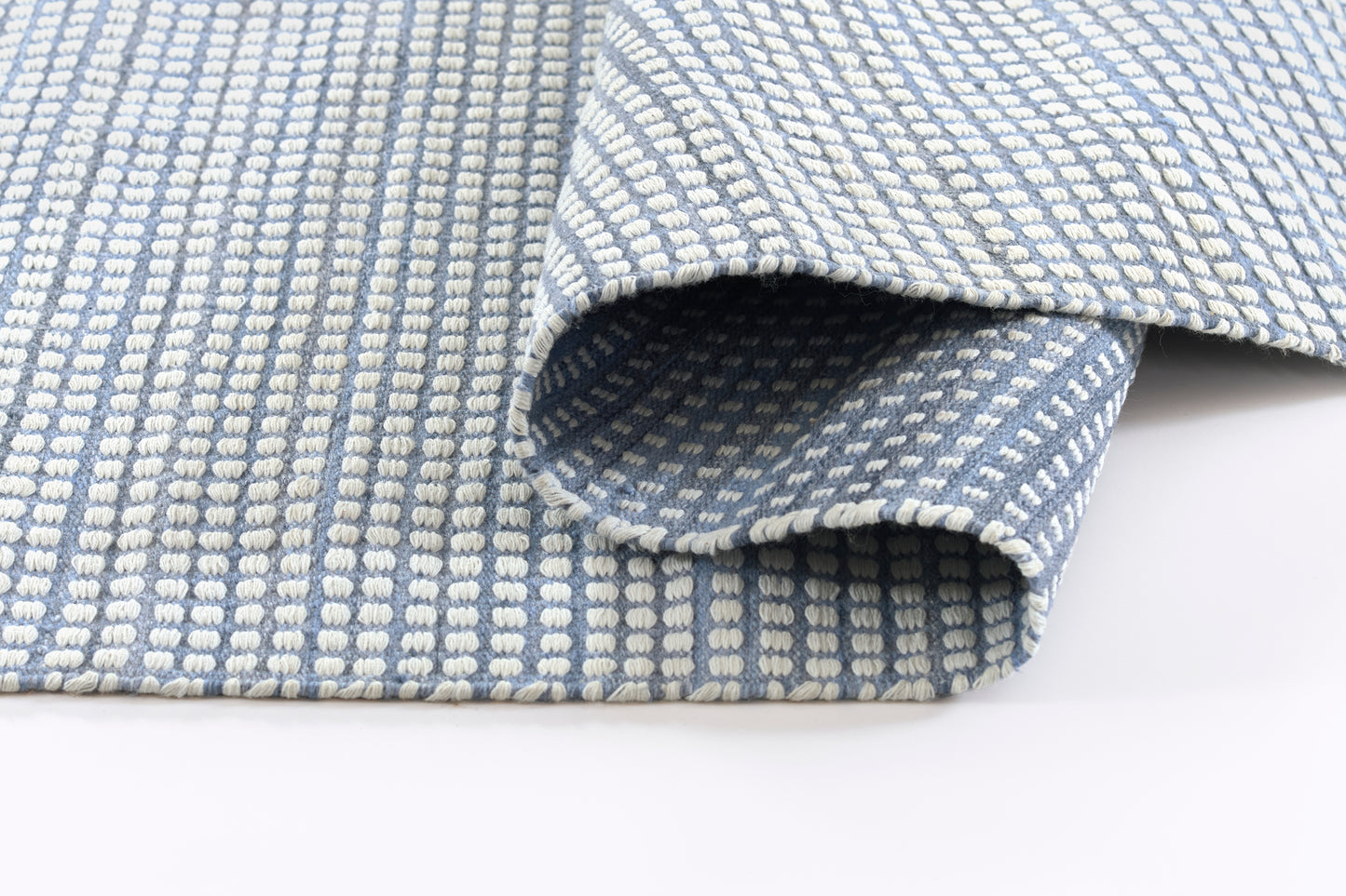 Blue woven rug featuring white dotted grid pattern, soft looped texture, rolled edge.
