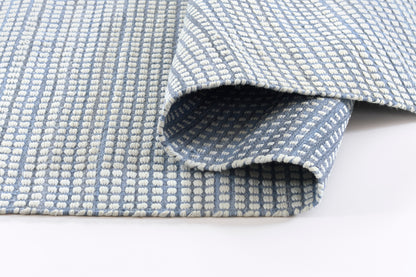 Blue woven rug featuring white dotted grid pattern, soft looped texture, rolled edge.