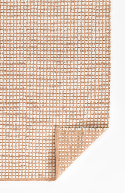 Blush pink woven rug with white dotted grid pattern; folded corner reveals soft, textured weave.