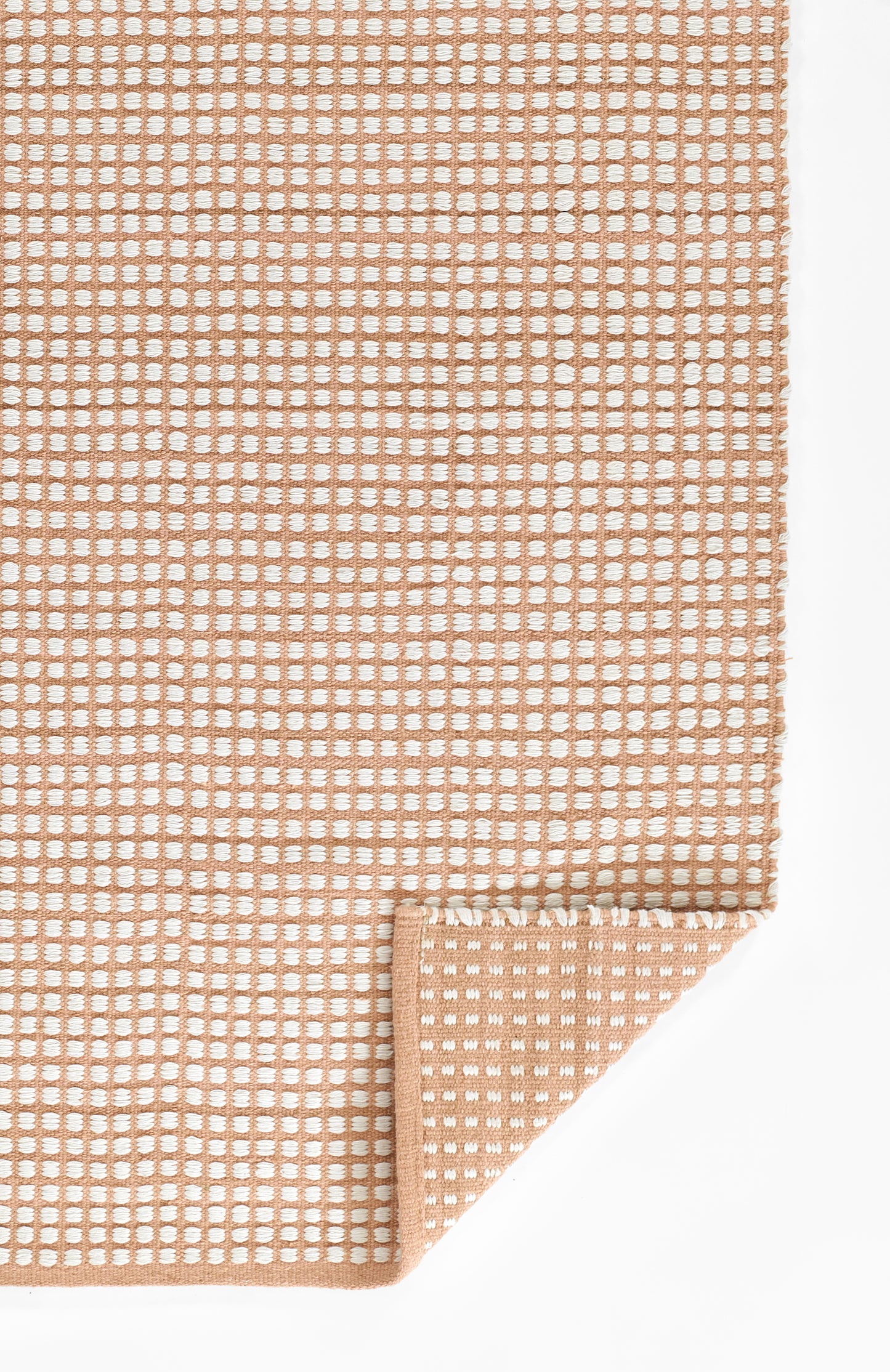 Peach-colored woven rug with white dot grid pattern, folded corner showing clean edge; modern geometric style.