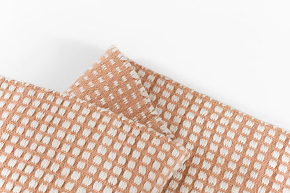 Peach pink rug with white rounded dot pattern, folded, with visible white stitched edges.