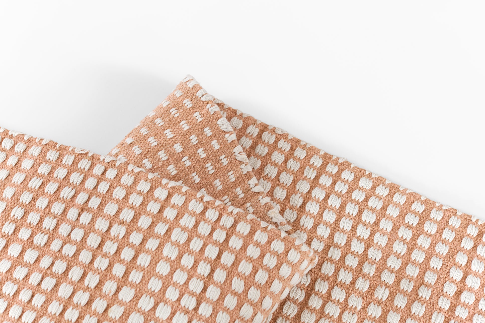 Peach rug runner with a white dotted pattern and white stitched edges.