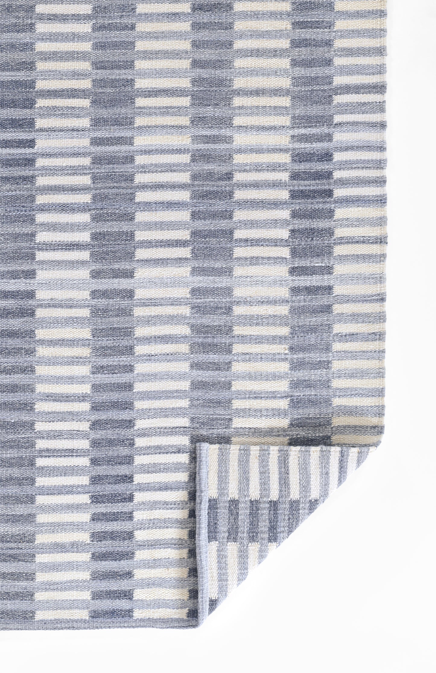 Blue & white striped woven rug with vertical bar pattern; folded corner reveals lighter reverse stripes.