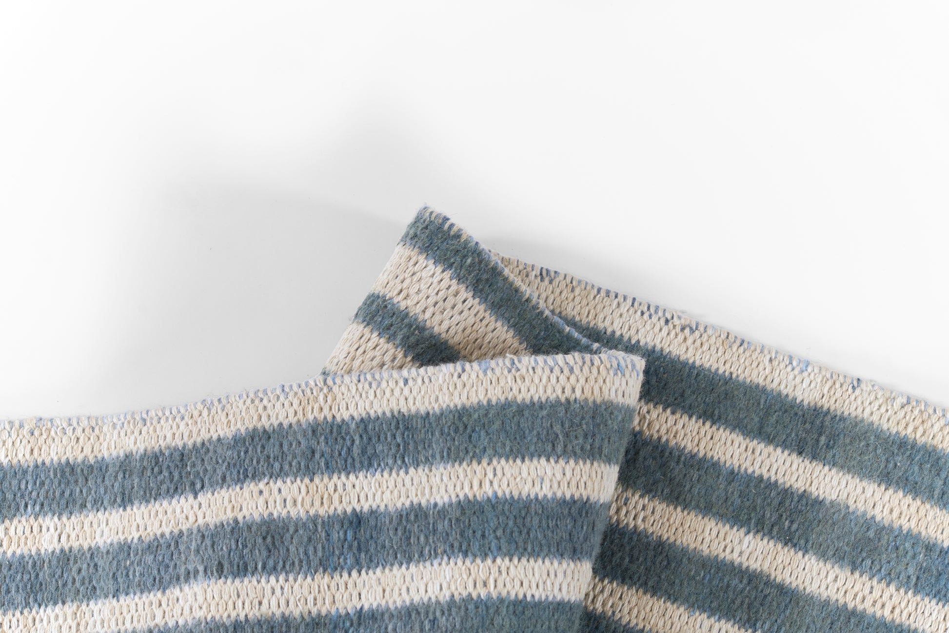 Blue and beige striped woven cotton rug with a chunky weave texture, folded pieces.