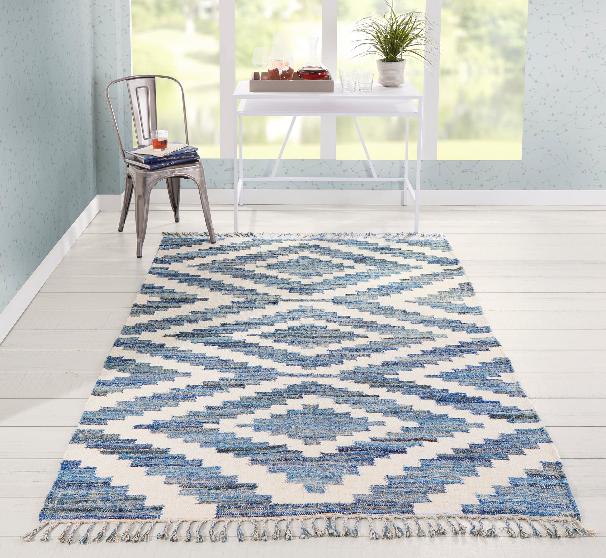 Blue and white geometric rug with fringe on mint-walled, bright room; metal chair, white desk, glassware, plant.