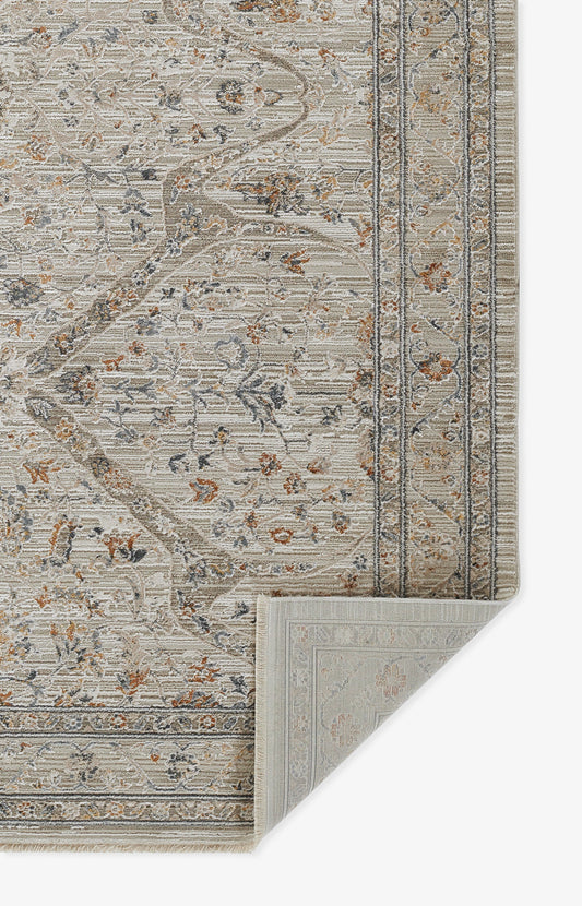 Beige oriental-style area rug with blue, rust floral motifs, bordered pattern; woven texture, folded corner shows underside and fringe edge.