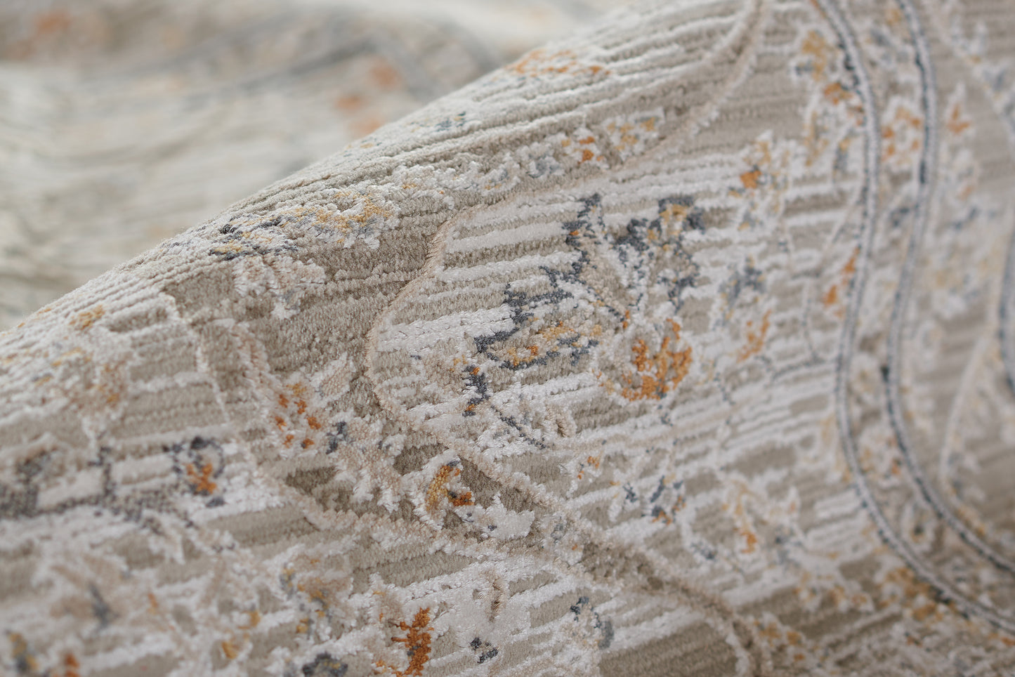 Beige patterned area rug with distressed floral motifs in blue-gray and orange, woven texture, rolled.