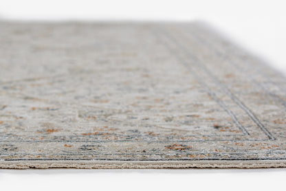Low-pile gray-blue area rug with subtle orange flecks and a bordered edge; fringe along the foreground.