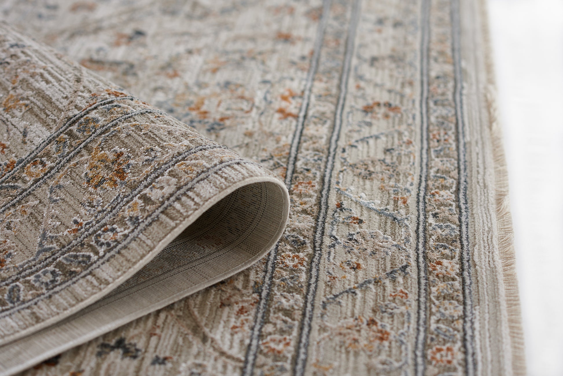 Beige oriental rug with blue and orange floral motifs, woven texture, rolled corner and fringe.