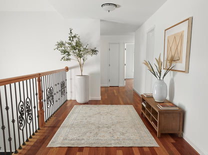 Bright hallway with wood floor, black iron railing, tall potted plant, light patterned rug, and wooden console with vase.