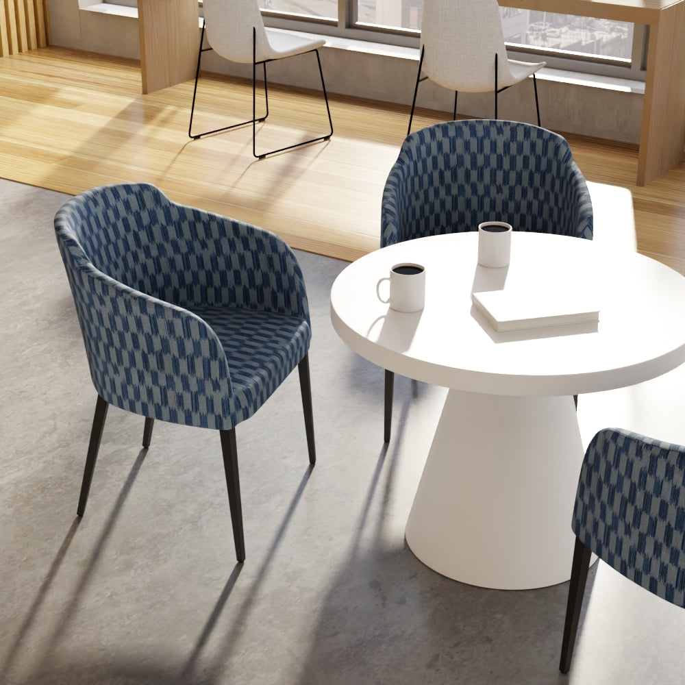 Modern seating area featuring indigo geometric fabric upholstery on chairs around a white round table with cups and a book