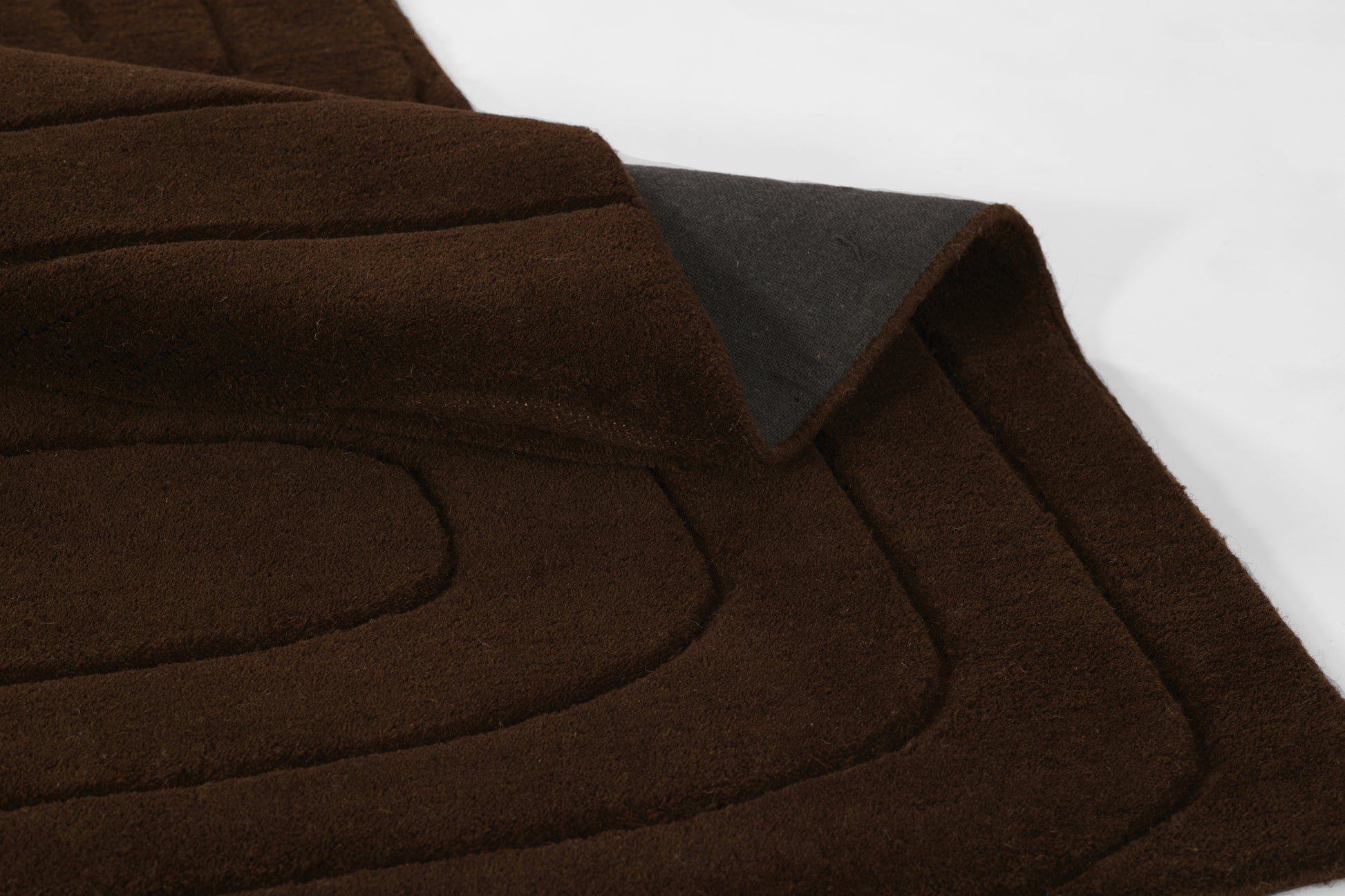 Dark brown suede-like quilted rug with curved stitched panels and folded edge detail, 5' x 8'.