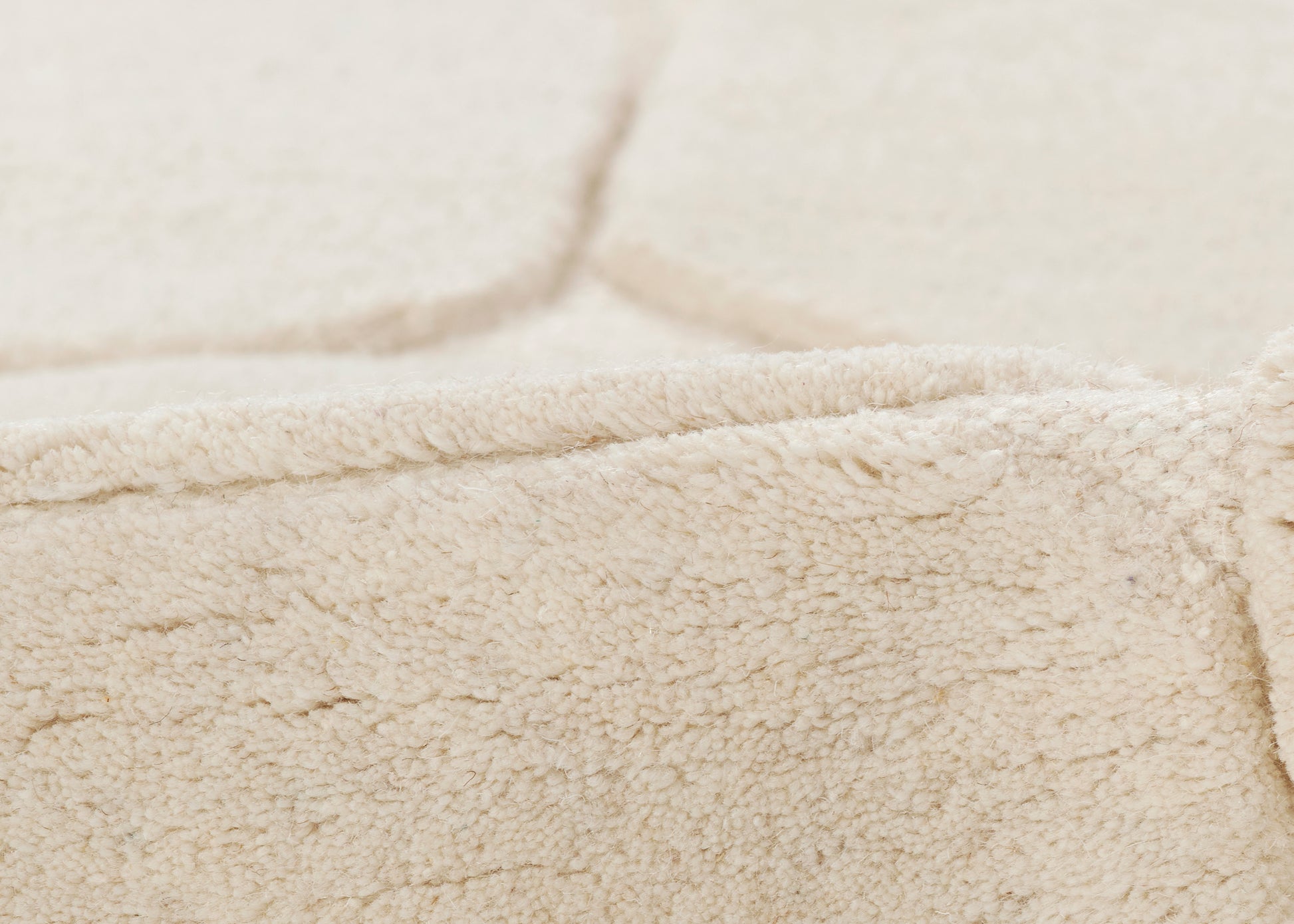Beige sherpa fleece fabric close-up with folded edge and soft, fluffy pile.