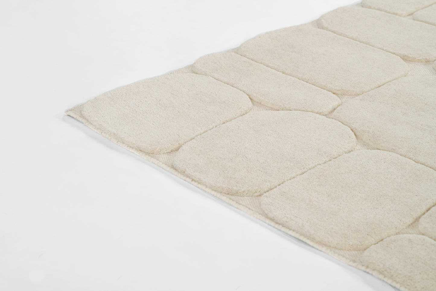 Beige plush rug with rounded tufted panels; soft textured surface, cozy modern design.