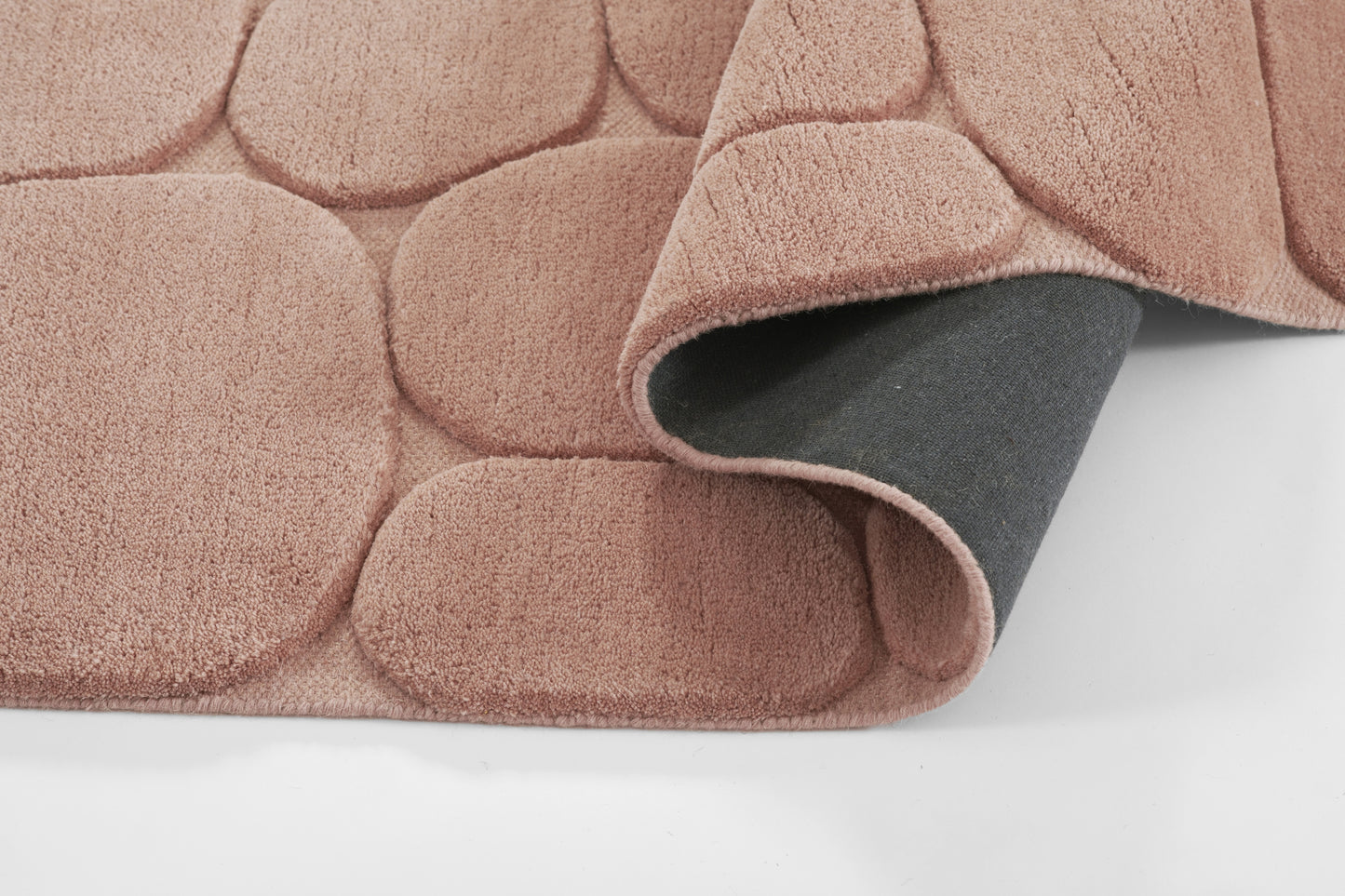 Soft pink plush rug with circular pebble pattern; curled corner reveals gray underside.