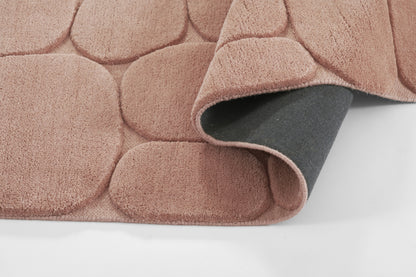 Soft pink plush rug with circular pebble pattern; curled corner reveals gray underside.