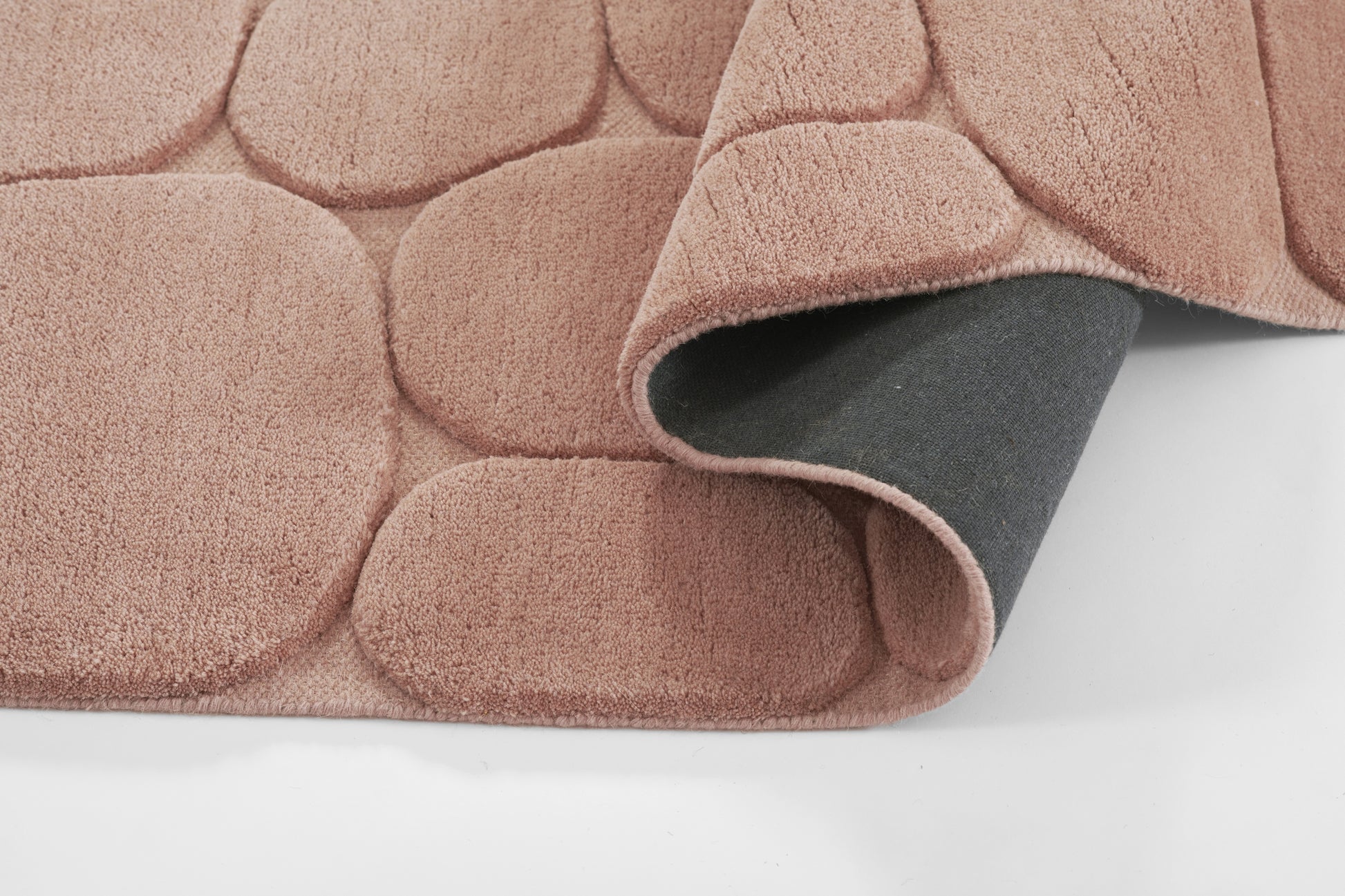 Soft pink plush rug with rounded bubble tuft pattern, rolled corner reveals gray underside.