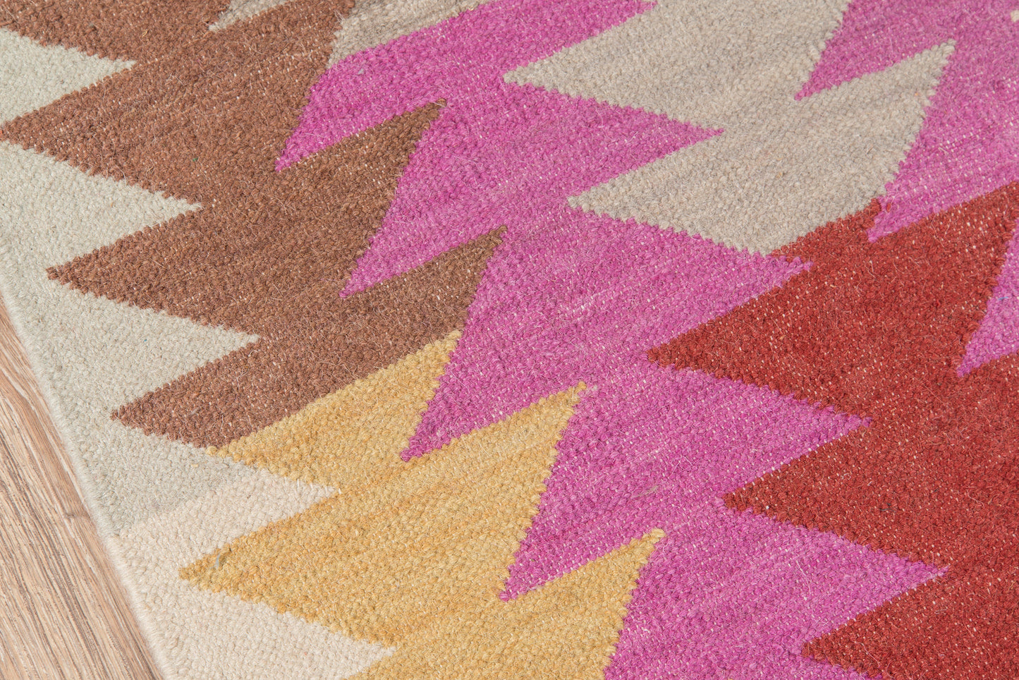 Geometric woven rug with bold pink, mustard yellow, brown and red chevron triangles on a beige base.
