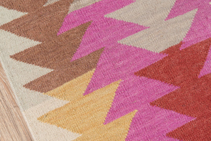 Geometric woven rug with bold pink, mustard yellow, brown and red chevron triangles on a beige base.