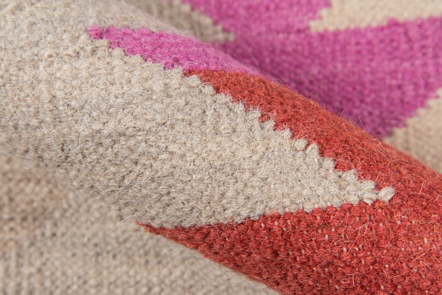 Close-up of a thick wool rug with beige base, red chevron stripe and pink accents.
