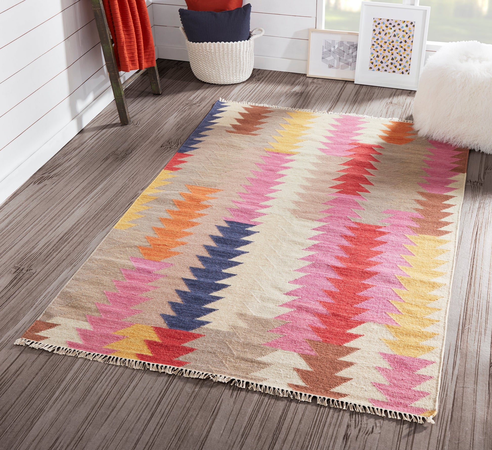 Woven kilim-style rug with multicolor zigzag chevrons on a beige background, in a bright cozy room.