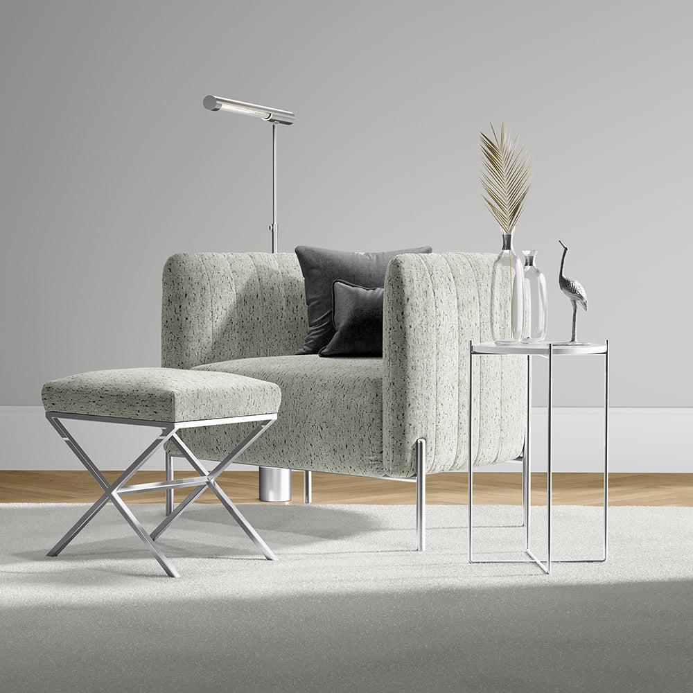 Light textured gray-green armchair with matching ottoman and chrome legs, paired with glass side tables and modern decor.