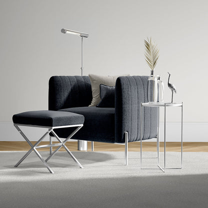Velvet dark gray sofa with beige and navy cushions, chrome X-legs ottoman, glass-top side tables, and slim floor lamp.