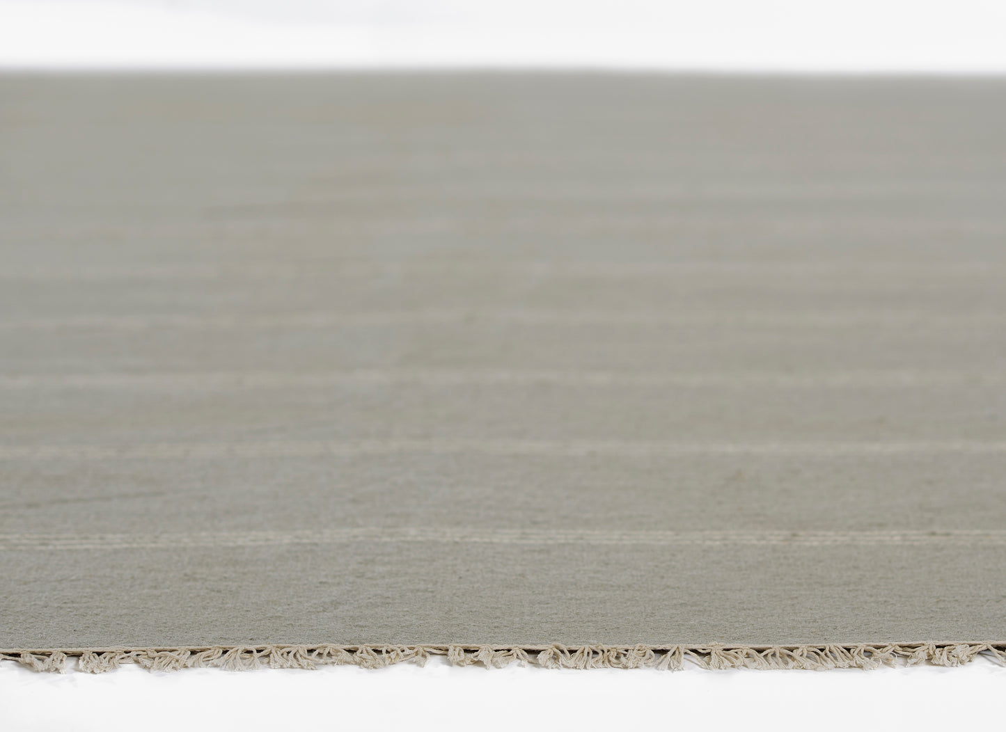 Neutral beige-gray flat-weave rug with a fringe along the bottom edge.
