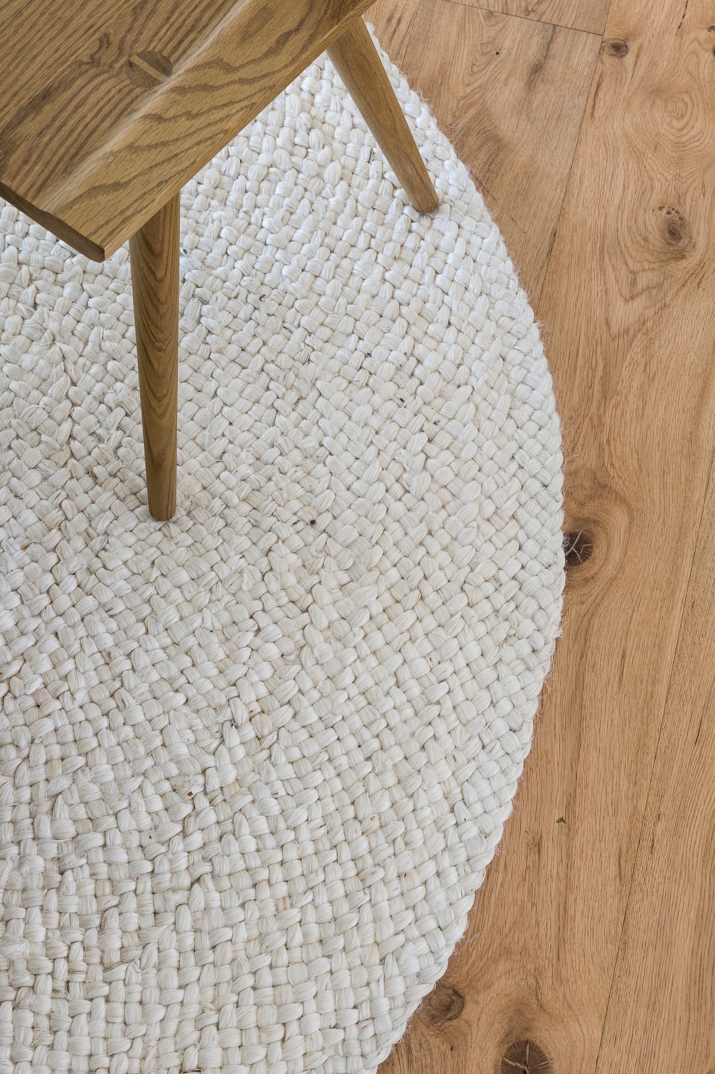 Rectangular cream woven jute rug with light beige tones under a wooden table leg on an oak floor (8' x 11').
