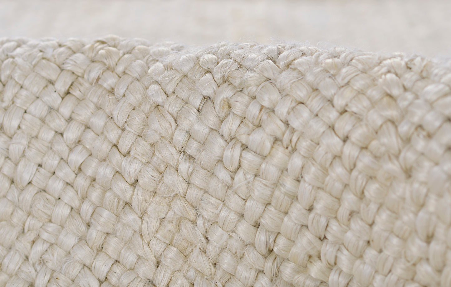 Close-up of cream braided jute weave; thick, chunky fibers create a natural rustic texture for baskets or bags.